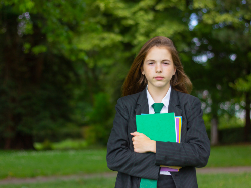 Schoolgirl holding folders, standing in front of trees