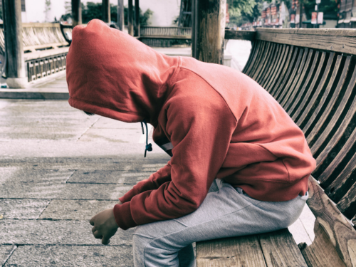 Side view of boy slouched forward on bench with his hoodie pulled up